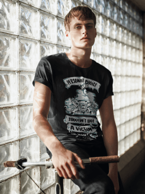 A Young male model posing with a bike and leaning against a window wearing a black organic T-shirt with illustraion of a live pig in a sandwich and the wording "personal choice shouldn't have a victim