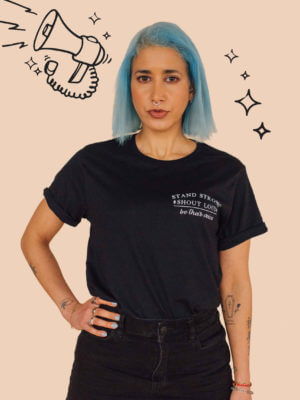 A blue haird model standing against a wall wearing Eco-ethical brand Viva La Vegan's black "Silence is not a option" t-shirt.