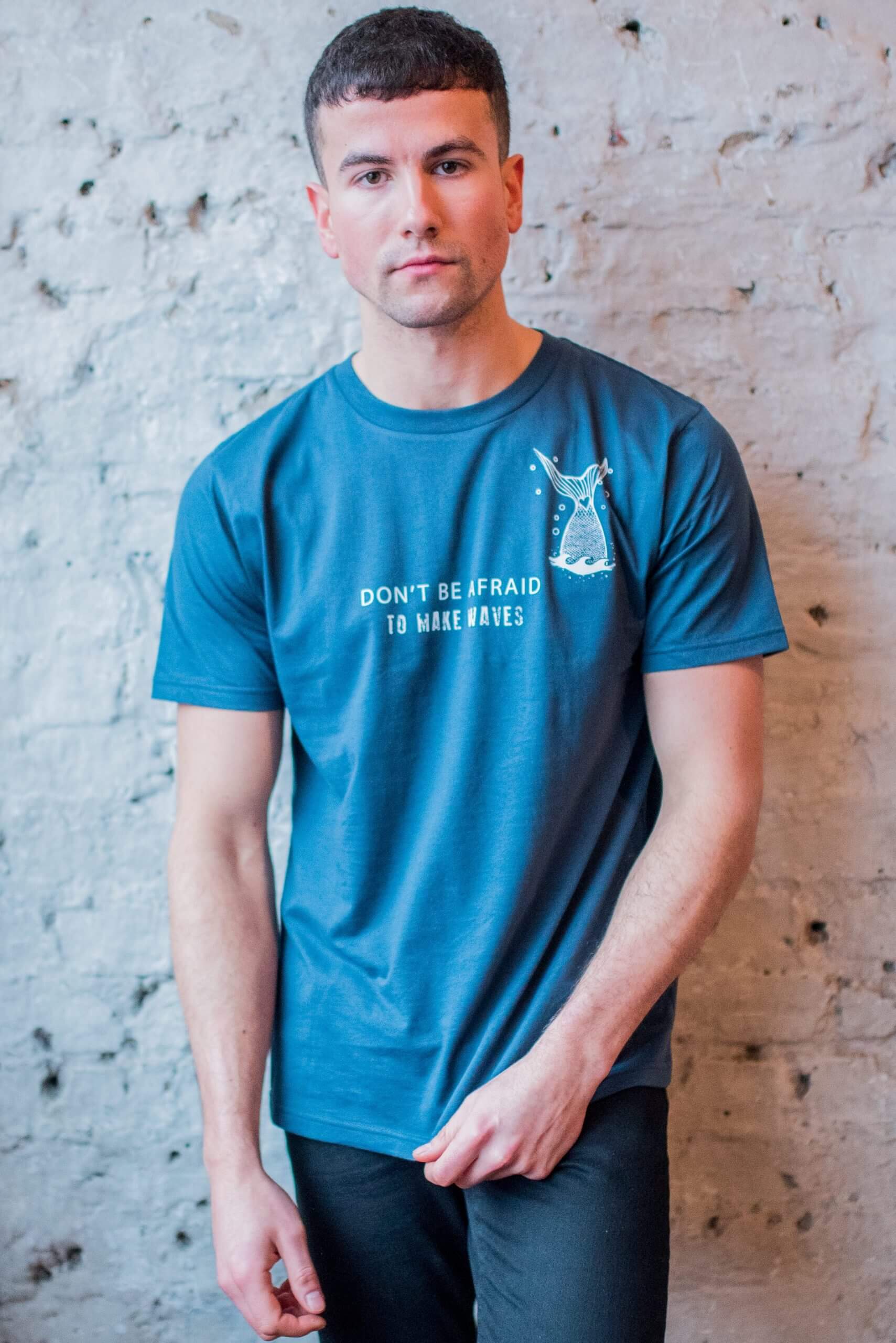 Male model posing against a brick wall wearing a denim blue t-shirt with marine themed design on the front. Designed by eco-ethical award winning Viva La Vegan.