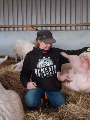 Sasha sat stroking a pig wearing a black hoodie with white print & hot pink trims. By Viva La Vegan. Fund raising for Beneath The Wood Sanctuary
