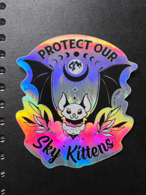 Sky Kittens holographic sticker on a black note book. by eco ethical brand Viva La Vegan