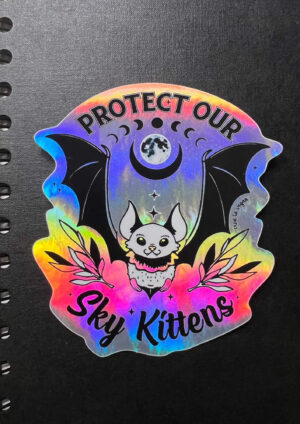 Sky Kittens holographic sticker on a black note book. by eco ethical brand Viva La Vegan