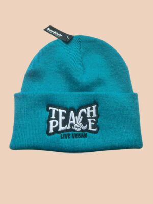 Flatlay photo of a cuffed beanie in petrol colour with a black and white embroidery 'Teach Peace - Live Vegan.