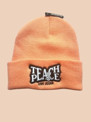 Flatlay photo of a cuffed beanie in Blush colour with a black and white embroidery 'Teach Peace - Live Vegan.