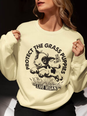 Cropped image of a woman wearing a unisex sweatshirt with crew neck, inset sleeves , torso print 'Grass Puppies - Eat Only Plants- Live Vegan - leaping cow print. Butter Colourway