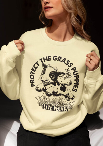 Cropped image of a woman wearing a unisex sweatshirt with crew neck, inset sleeves , torso print 'Grass Puppies - Eat Only Plants- Live Vegan - leaping cow print. Butter Colourway