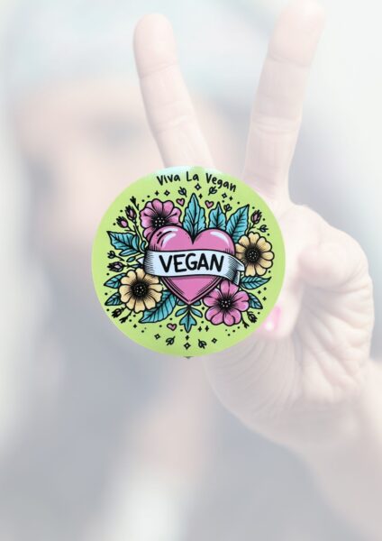 Photo of a greaan round window sticker with a pink heart with a ribbon banner saying Vegan, Surrounded in pretty illustrated flowers