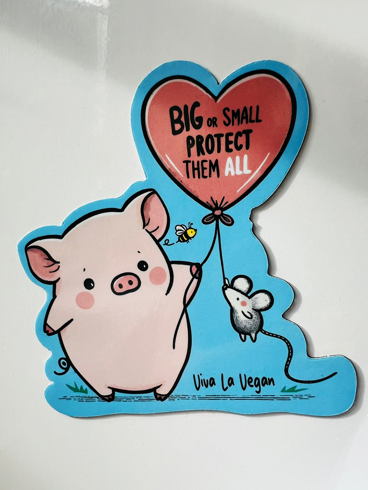 A custom shaped magnet of a pig and a mouse holding a balloon with the writing 'Big or small - protect them all' on a blue background