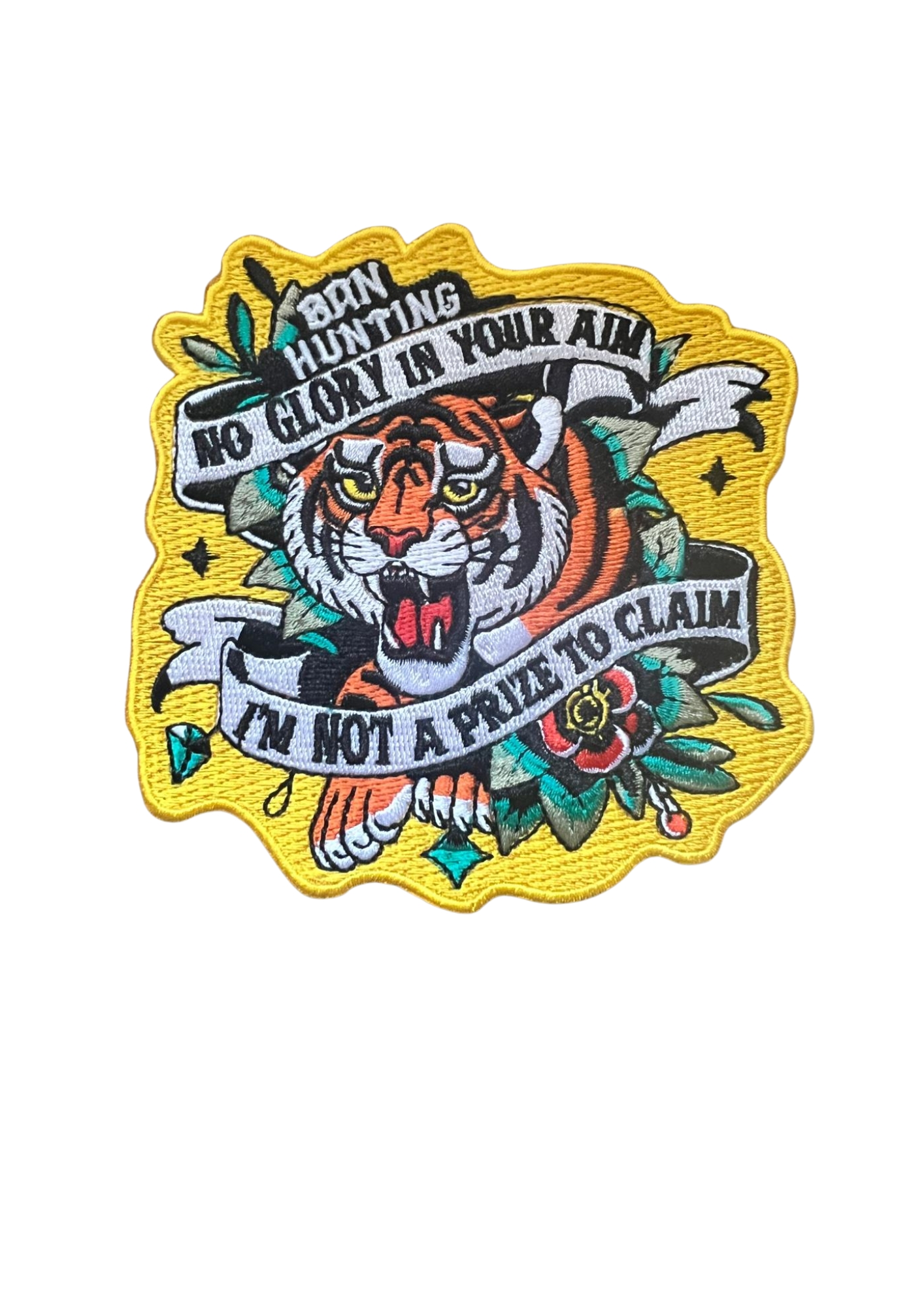 Embroidered patch featuring a roaring tiger surrounded by floral motifs and bold banners. Text reads: “Born Hunting / No Glory In Your Aim / I'm Not A Prize To Claim.” Vivid colors and yellow border emphasize themes of resistance and animal dignity.